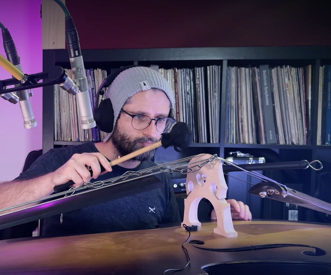 Lukas Fretz mit Kopfhörern spielt mit einem Schlägel auf einem präparierten Instrument, vor ihm Mikrofone